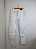 Load image into Gallery viewer, Light blue jeans hanging on a wooden hanger against a plain wall.
